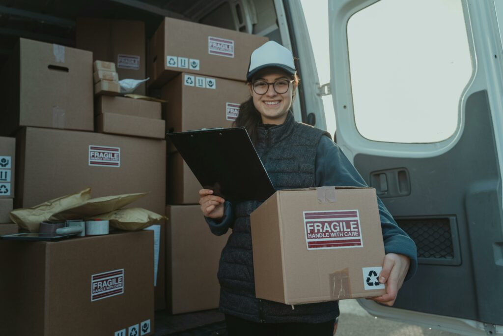 A cheerful delivery woman prepares parcels inside a van, ensuring careful handling.